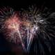 Colourful fireworks burst in the night sky with multiple streaks and sparks radiating outward.