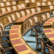 Rows of wooden chairs with cane backs and leather desks in a legislative chamber